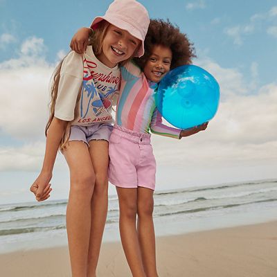 Girls wearing summer holiday clothing. Shop kids’ holiday clothes
