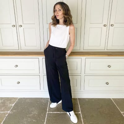 Woman wearing white tank, black slouchy trousers and white trainers