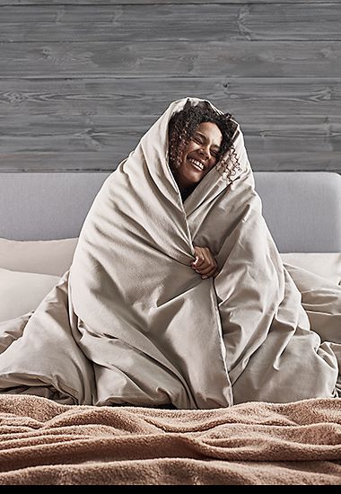 Woman sitting on bed, wrapped in a duvet