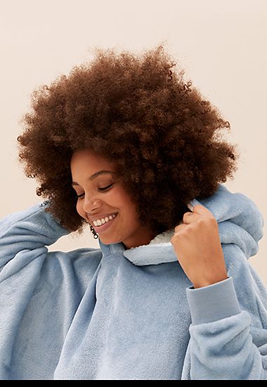 Woman wearing blue fleece hooded blanket. Shop women’s fleece nightwear
