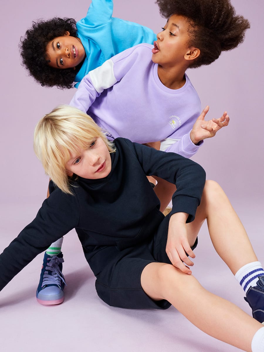Three chikdren wearing colourful sweatshirts and shorts. Get 3 for 2 on selected kids’ clothing now