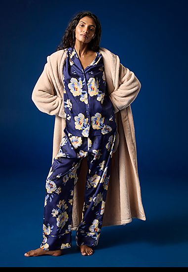 Woman wearing navy floral-print satin pyjamas and ivory borg-lined dressing gown. Shop the dressing gown
