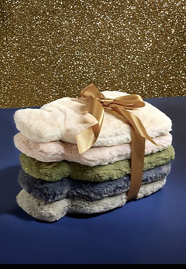 Stack of five faux fur hot water bottles tied with gold ribbon. Shop now