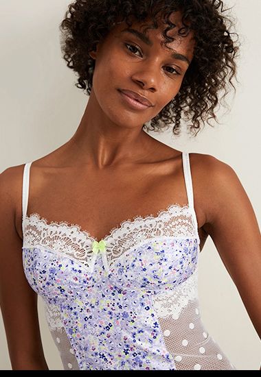 Woman wearing lilac floral camisole with white lace and green bow. Shop now. 