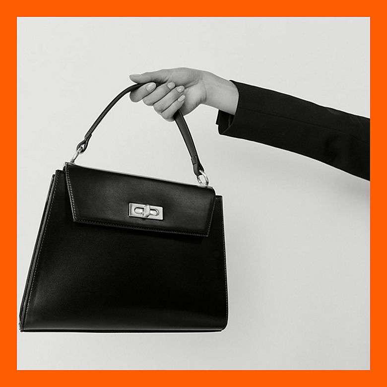 Woman holding a black faux-leather structured handbag. Shop capsule clothing 