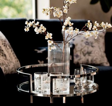 Glass ribbed vase with floral stems and assorted cut-glass tumblers on a silver drinks trolley. Shop the vase