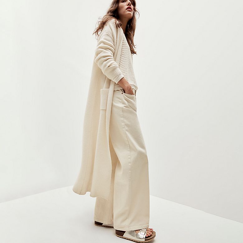 Woman wearing long cream cardigan, cream trouser and metallic sandals. Shop women’s new-in 