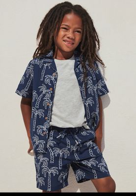 Boy wearing navy palm-print shirt and matching shorts. Shop boys’ shorts