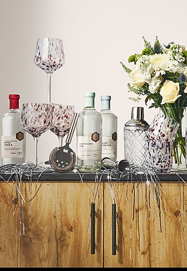 A selection of drinks, barware, glassware and flowers on a sideboard. Shop glassware