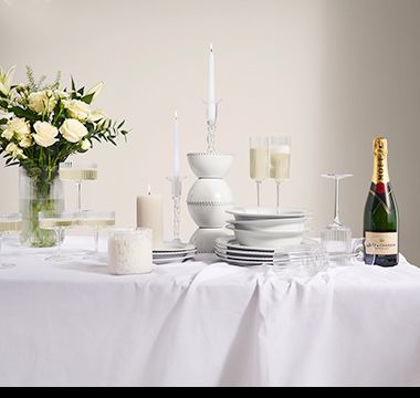 Table with a selection of white dinnerware, glassware and candles. Shop tableware