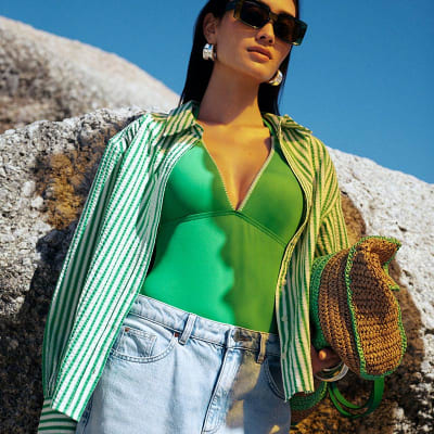 Woman wearing a green swimsuit, green striped shirt and light-blue wide-leg jeans. Shop women’s summer clothing 