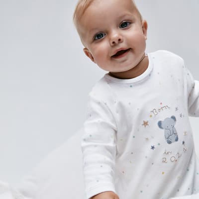 Baby wearing white sleepsuit. Shop sleepsuits