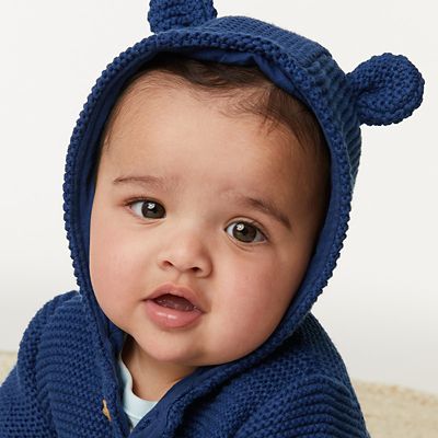 Baby wearing navy knitted cardigan with hood and ears. Shop now 
