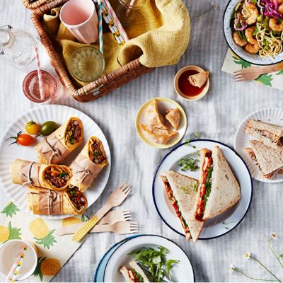 A selection of sandwiches and wraps arranged picnic-style, with a hamper on a blanket