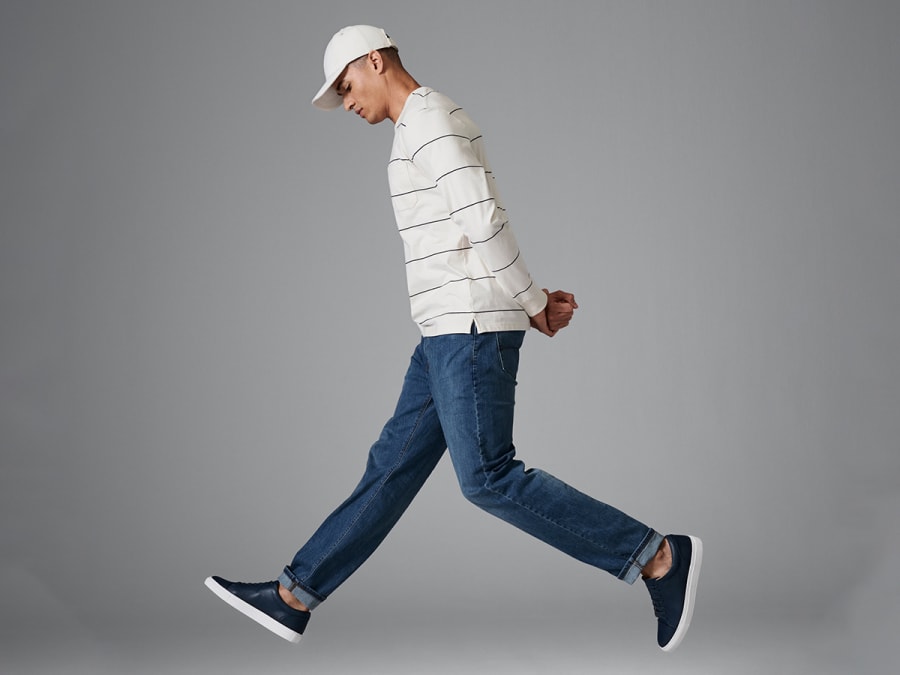 Man wearing dark-wash blue jeans, white long-sleeve top, white cap and black trainers 
