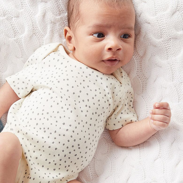 Baby wearing cream bodysuit with grey dot pattern. Shop now