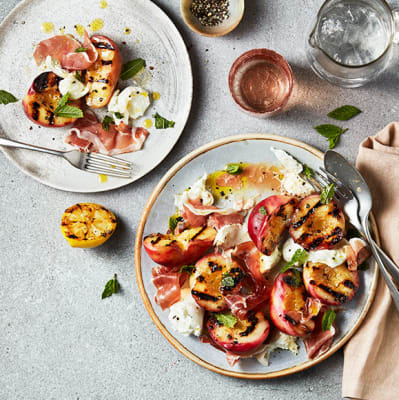Two plates of stone fruit salad with fresh peaches, mozzarella and prosciutto