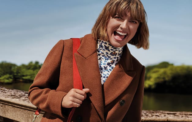 Woman wearing a tan coat and cream floral polo neck