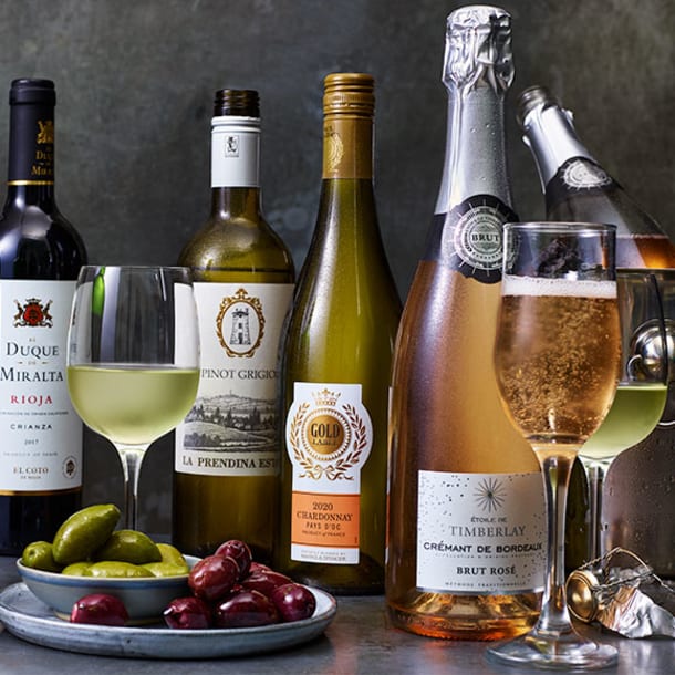 Various glasses and bottles of wine with plate of olives and caperberries