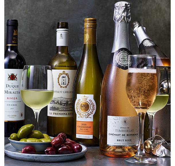 Various glasses and bottles of wine with plate of olives and caperberries