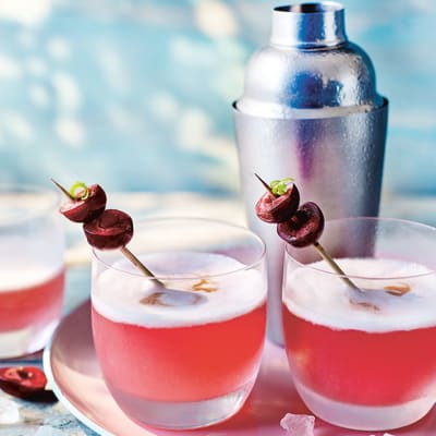 	 Two cherry pisco cocktails with a cocktail shaker in the background
