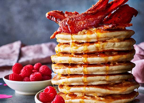 A stack of pancakes topped with bacon and maple syrup