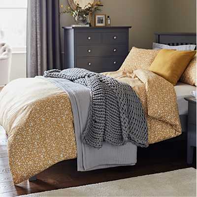 Bed with mustard printed bedding and grey throws