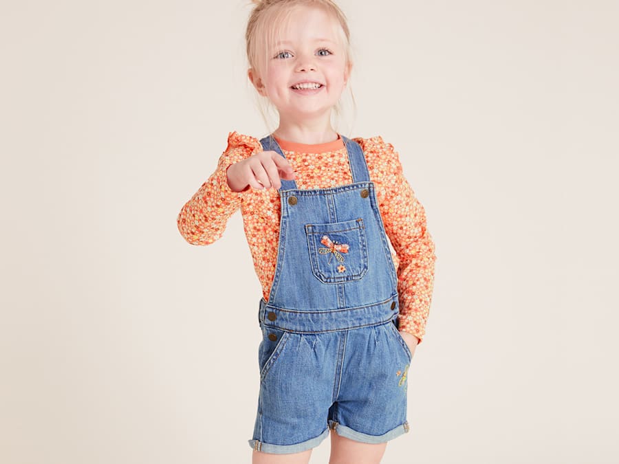 Girl wearing denim dungarees and orange printed top