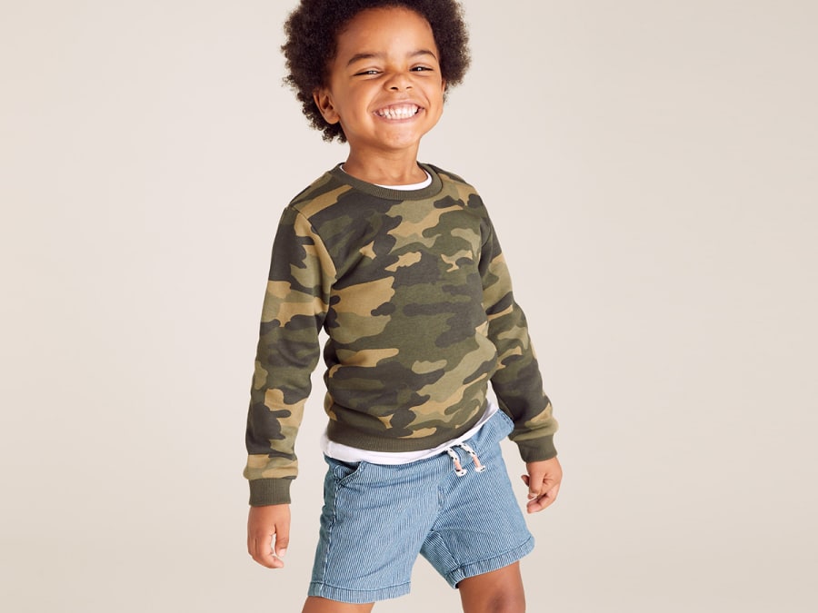 Boy wearing camo-print sweatshirt and denim shorts