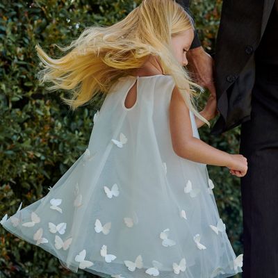 Girl twirling, wearing a white sleeveless dress with butterfly detailing