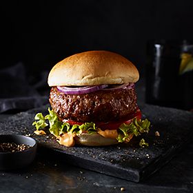Our Best Ever burger on a chopping board with a pot of pepper