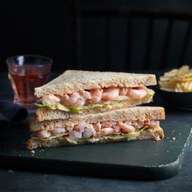 Our Best Ever prawn sandwich on a chopping board with crisps and a drink