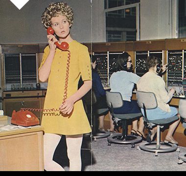 Woman wearing a yellow mini shift dress and white tights in the office, 1970
