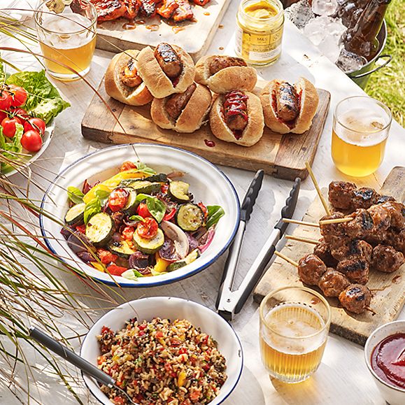 A barbecue feast with hot dogs, kebabs, pineapple streakies, salads and glasses of beer