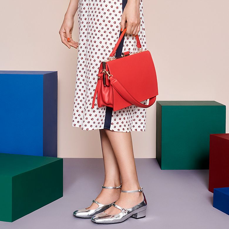 Model wears printed dress with silver Mary Janes and a red bag