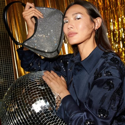 Woman wearing black sequinned shirt and holding silver sequinned bag. Shop partywear