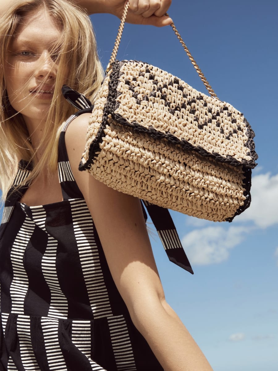 Woman holding straw shoulder bag. Shop handbags